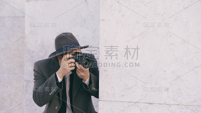 年轻的狗仔队男子在帽子拍摄名人的特写镜头，而间谍在墙后