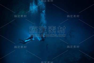 两名潜水员在坑的底部用手电筒和气泡