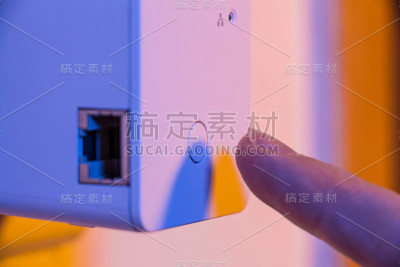 男子将手指按在WiFi中继器的WPS按钮上，该按钮位于墙上的电源插座上