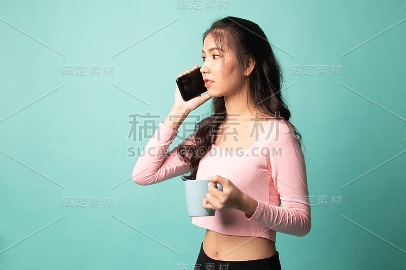 年轻的亚洲女人拿着手机和咖啡杯。