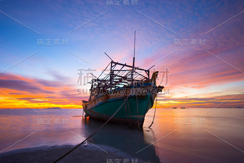 美丽的剪影渔船搁浅在低潮海沙，戏剧性的天空黄昏的背景