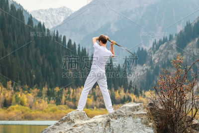 一个年轻人站在一块大石头上，手里拿着一把日本剑。