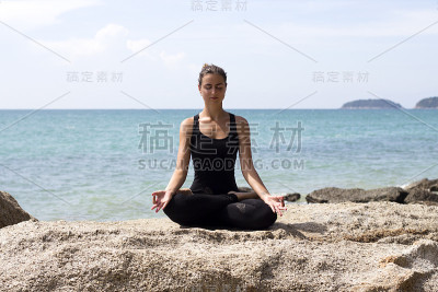 瑜伽女人在海边和岩石附近的海滩上摆姿势。普吉岛