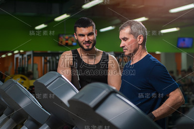 在健身房和私人教练一起工作的资深男士。