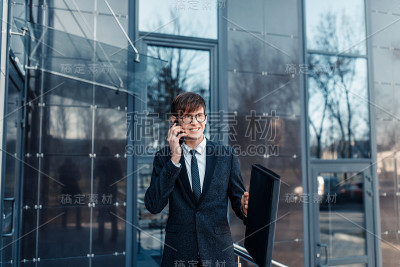 戴着眼镜的时尚商人在商务中心的玻璃大楼附近打电话