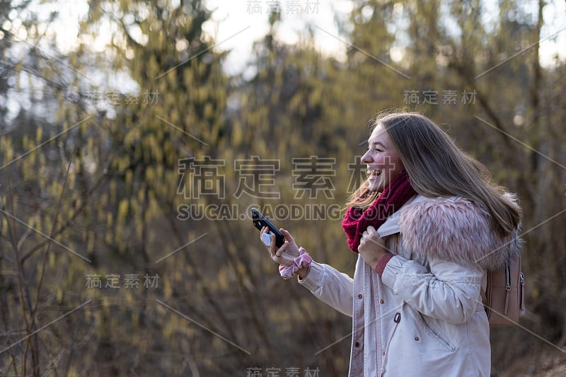 一个白人女孩微笑着拿着她的智能手机在户外