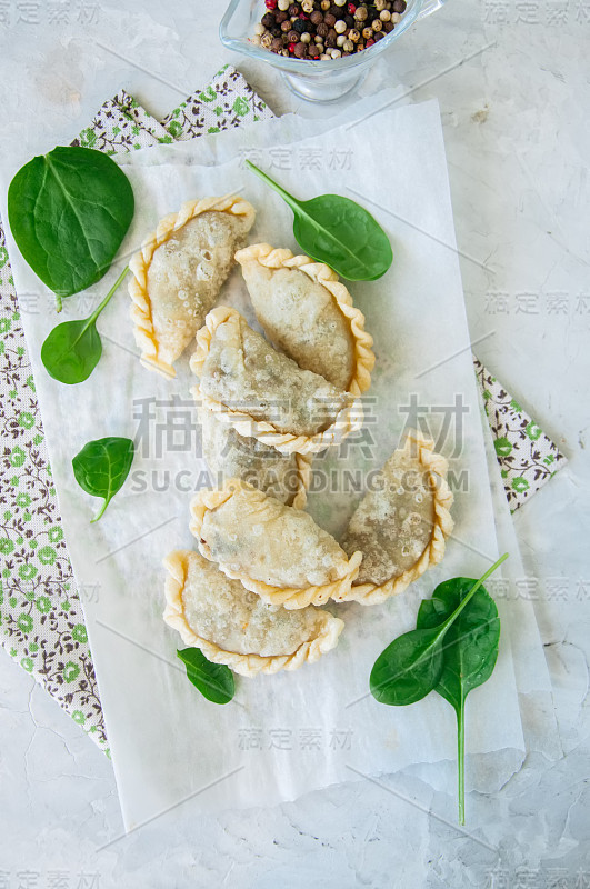 油炸美味馅饼-在白色的背景上加菠菜的手馅饼。俯视图和复制空间。