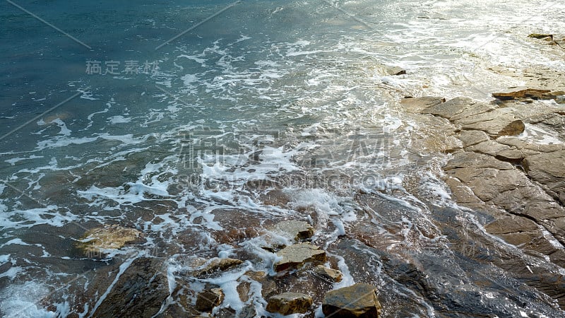 绿色的海浪拍打着岩石的海岸，变成白色的泡沫