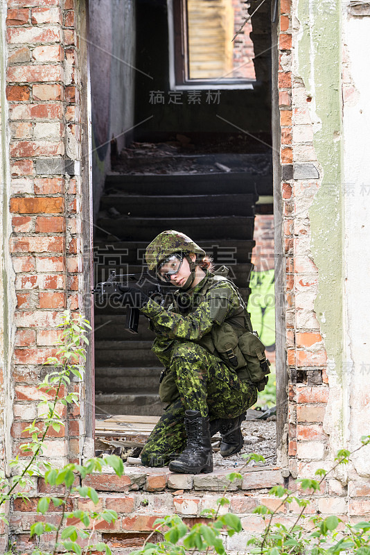 身着迷彩服的武装女子的肖像。年轻的女兵用枪观察。儿童兵与枪在战争壁炉，房子废墟的背景。军民观念，军民