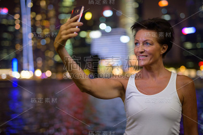 在新加坡滨海湾，一个成熟的女人在晚上用手机自拍