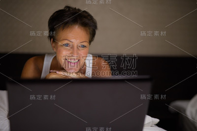 快乐成熟的女人晚上在酒店房间用笔记本电脑