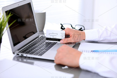 商业妇女的手使用信用卡和笔记本电脑的特写
