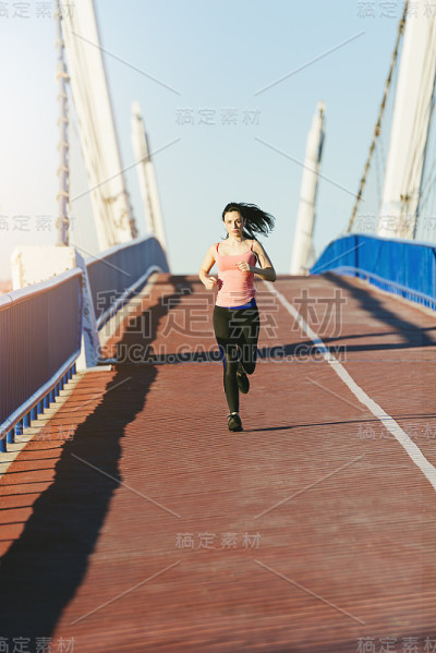 年轻的健身女运动员在城市大桥上跑步。