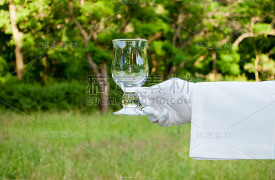 一个戴着白手套的服务员的手在露天端着一杯水