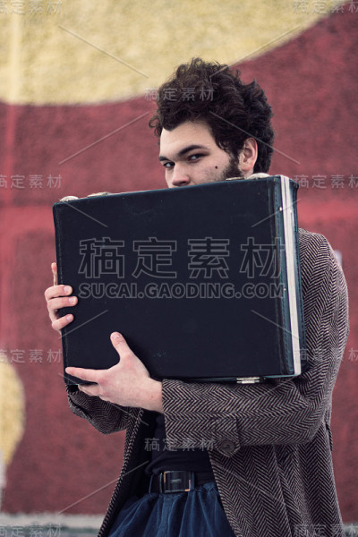 卷毛男人拿着一个手提箱，看着摄像机