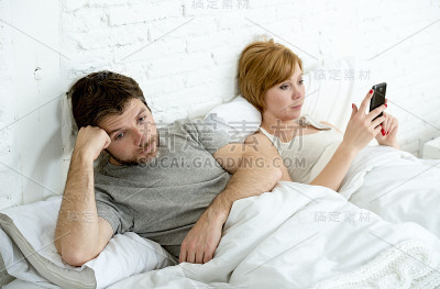 夫妻在床上丈夫沮丧的妻子使用手机