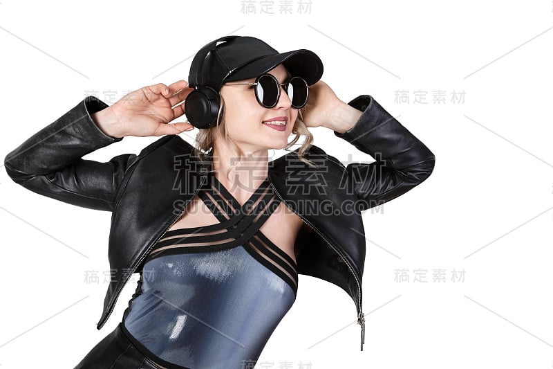 年轻美丽的金发女子穿着黑色皮夹克和帽子，戴着黑色无线耳机听音乐，