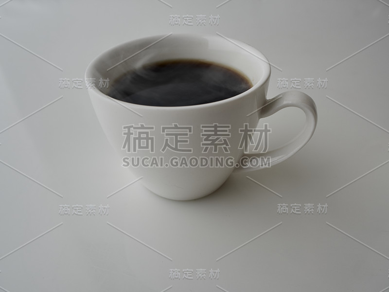 白色桌子上白色杯子里的热黑咖啡有烟