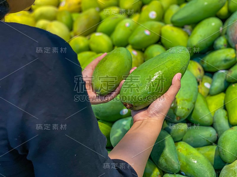 在热带水果市场，一个妇女拿着和挑选着青芒果