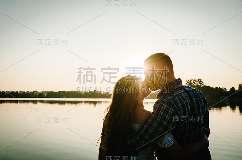 一对夫妇的剪影。一对年轻的情侣在春天的夕阳下亲吻拥抱。一个男人和一个女人在太阳的背景。爱和家庭的概念