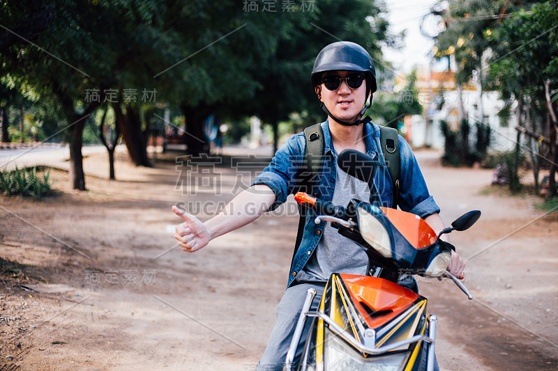 年轻快乐和英俊的男性摩托车手骑摩托车给大拇指和积极。