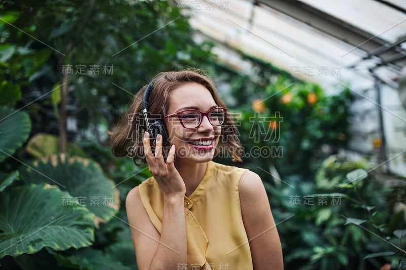 年轻女子戴着耳机站在植物园的温室里。