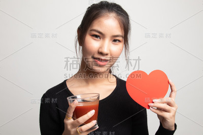 年轻的亚洲女人，喝着番茄汁和红心。