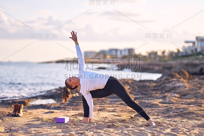 年轻美丽的女运动员练习瑜伽。教练在沙滩上教战士摆姿势