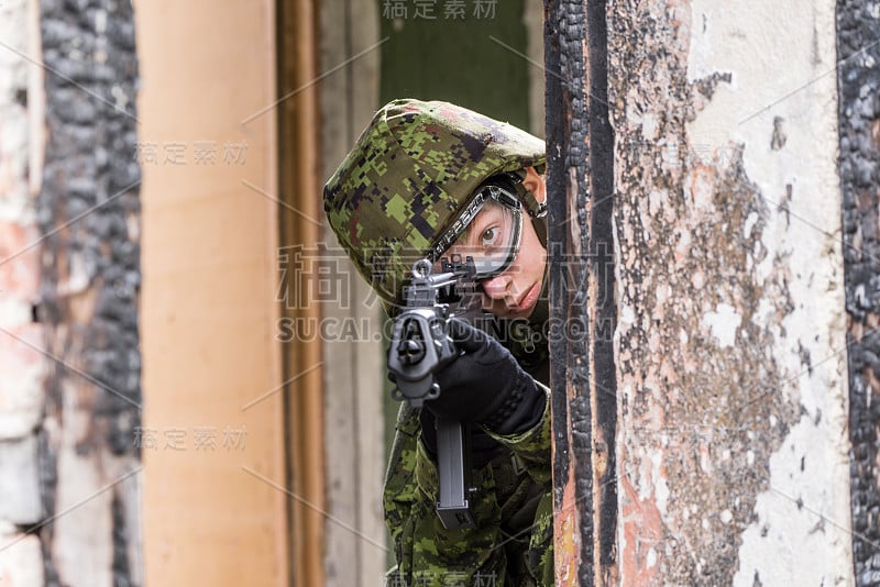 身着迷彩服的武装女子的肖像。年轻的女兵用枪观察。儿童兵与枪在战争壁炉，房子废墟的背景。军民观念，军民