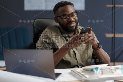 年轻的美国黑人微笑着使用智能手机。快乐的商人使用手机应用程序，发短信，浏览互联网，看智能手机。使用移