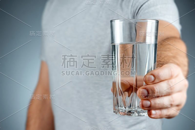 玻璃杯与纯矿泉水在男性的手特写在一个灰色的背景。药物治疗健康饮品