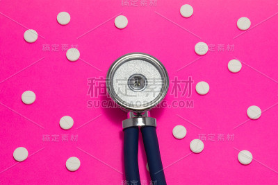 听诊器头部以粉红色为底色，周围点缀有圆点花纹的药丸或药片。照片概念诊断、治疗和预防各种疾病，用于医学