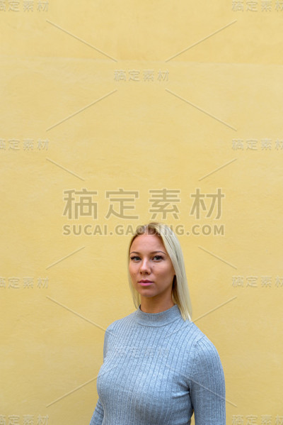 年轻美丽的女人靠在米色的墙上