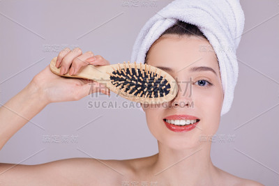 面带微笑的女孩裹着毛巾，拿着一把木梳子靠近她的眼睛。
