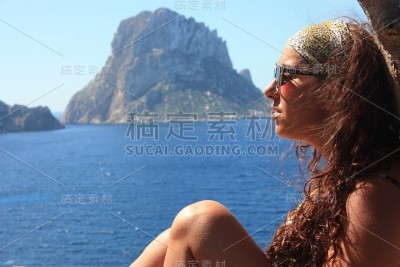 一个黑发白种女孩的暑假坐在树枝上欣赏埃斯韦德拉岛在卡拉霍特在伊比沙岛