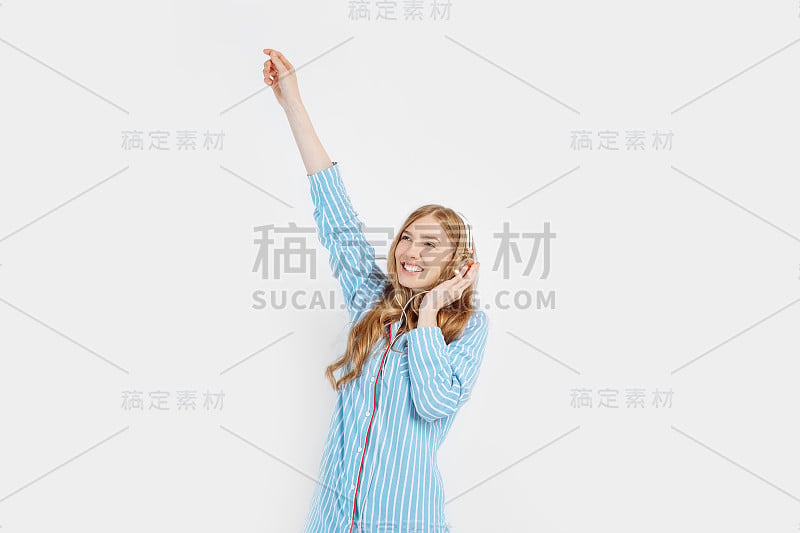 快乐迷人的年轻女孩穿着睡衣听音乐耳机上的白色背景