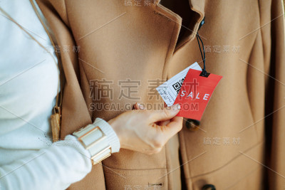 女人审视米色大衣上的价格标签的特写