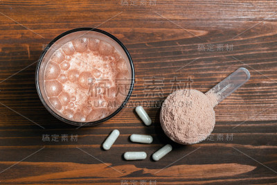 玻璃与乳清蛋白分离奶昔，蛋白粉勺，氨基酸和肌酸的白色胶囊木桌，俯视图