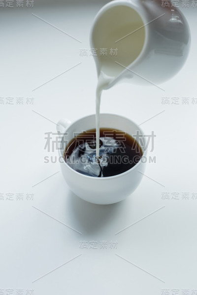 人们把牛奶从罐子里倒进白色桌子上的黑咖啡里