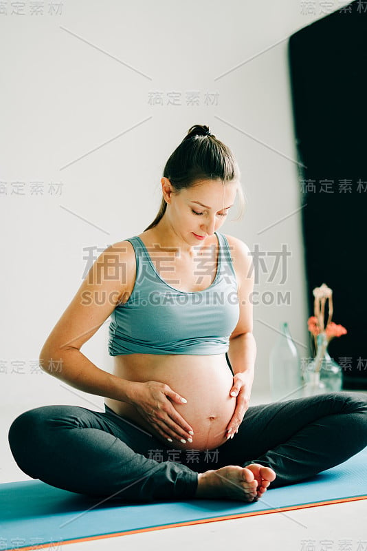 一个年轻漂亮的怀孕女孩穿着运动服在做瑜伽，在工作室的垫子上做体式小体式