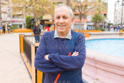 英俊的中年老人笑容开朗，幸福和积极的双臂交叉在城市城镇
