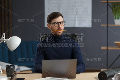 建筑师使用笔记本电脑在办公室工作。工程师对建筑方案进行思考，为建设项目寻找新的思路。长着胡须的英俊男
