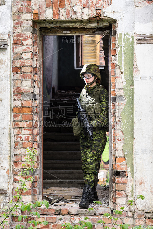 身着迷彩服的武装女子的肖像。年轻的女兵用枪观察。儿童兵与枪在战争壁炉，房子废墟的背景。军民观念，军民