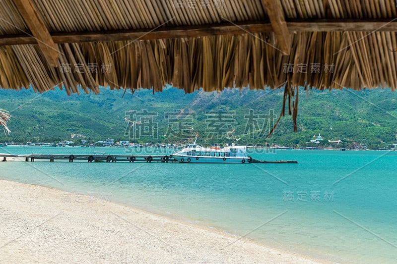 一艘大型游艇停泊在海湾的码头上，背景是群山