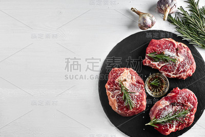 新鲜的生牛排配香草，大蒜，橄榄油，胡椒，盐和迷迭香在黑板上:里脊肉，Striploin，肋眼