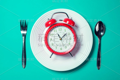 闹钟放在白色盘子上，勺子和叉子放在彩色背景上。饮食概念
