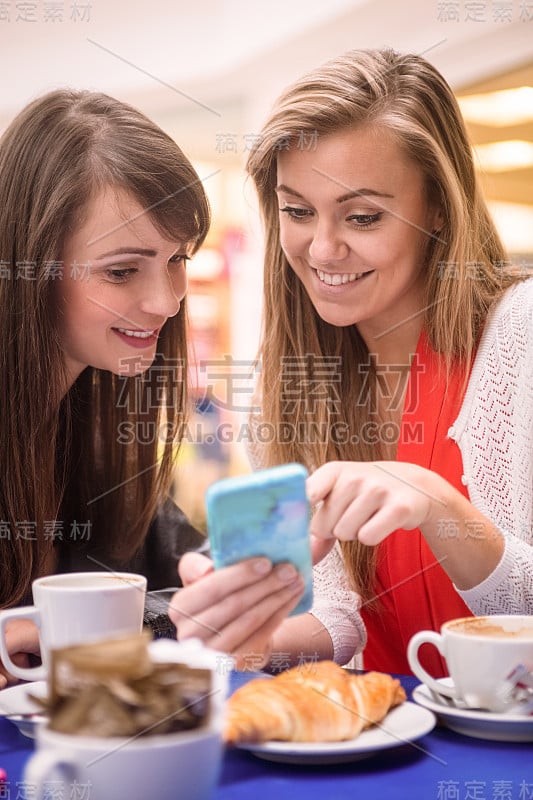 两个女人一边看手机一边吃着零食和咖啡