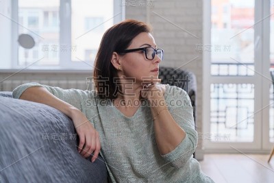 沮丧的成熟女人坐在家里的地板上