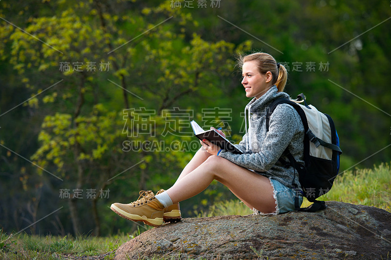 女子背包客写笔记徒步旅行在夏季的森林和停下来休息，旅游，徒步旅行，背包，旅游和人的概念