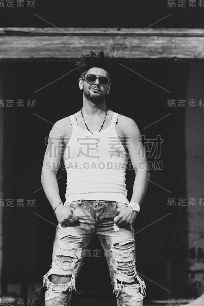 肖像英俊的男子在休闲服装摆姿势在废弃的地方，看向一边。黑白图像。城市人的概念。后期制作添加谷粒。